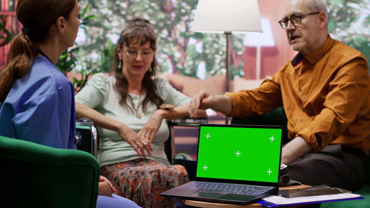 cuidador consultando a una anciana en silla de ruedas junto a la pantalla verde