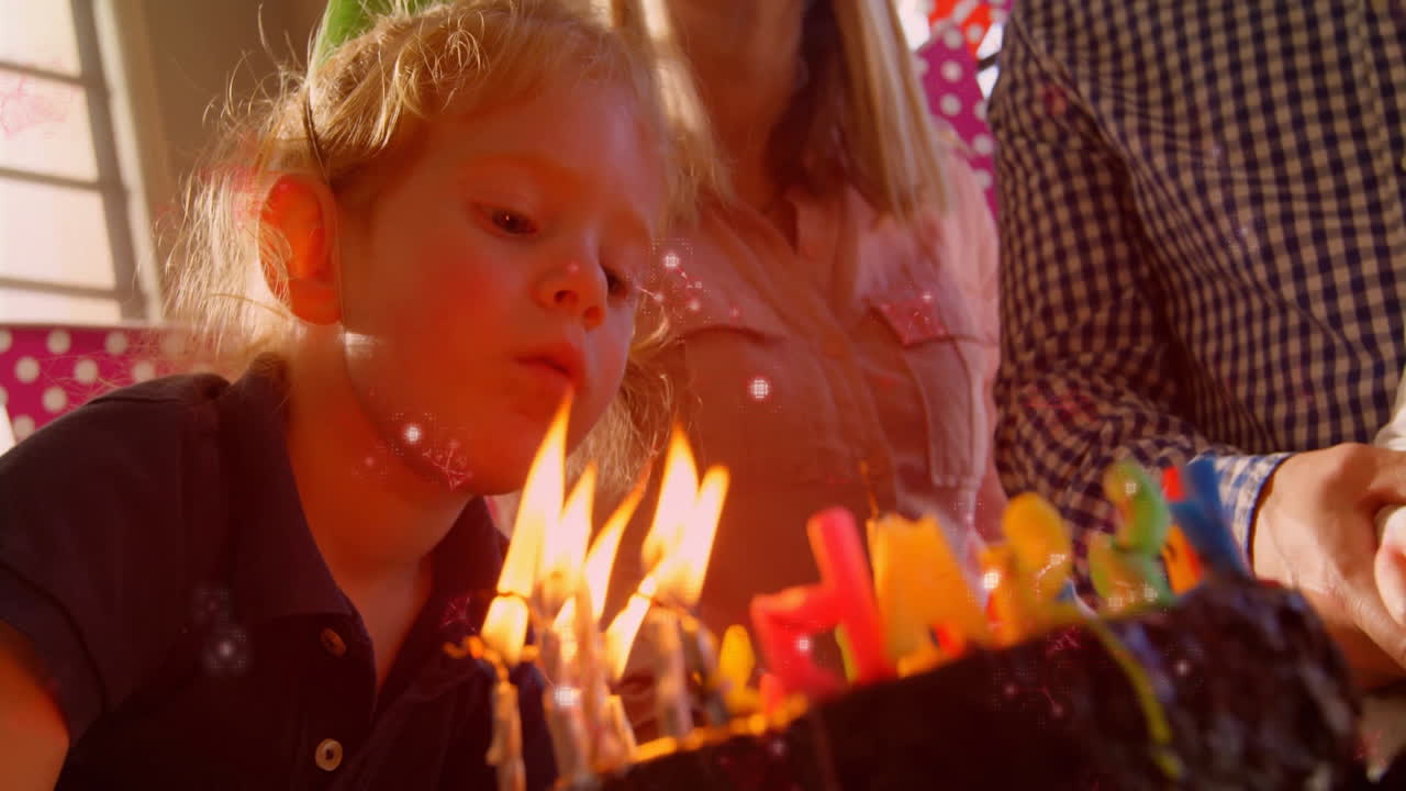 Blowing out candles on birthday cake, child surrounded by family in celebration