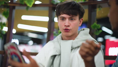white man looking at blurry phone screen shown by friend, facial focus on curiosity and confusion, indoor casual setting, close capture of reaction and interaction over shared media