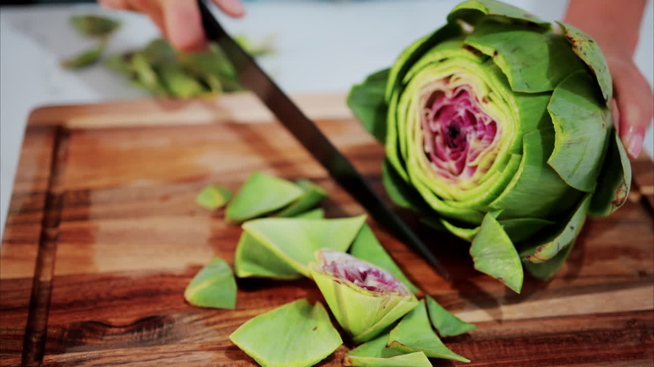 Woman cutting up an artichoke on a wooden cutting board in the kitchen