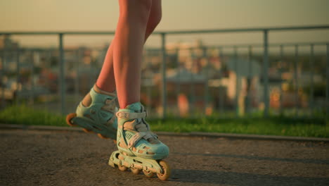 side leg view of person roller skating outdoors near iron railing under warm evening sunlight, rollerblades, with blurred cityscape and buildings illuminated by soft sunset glow in background