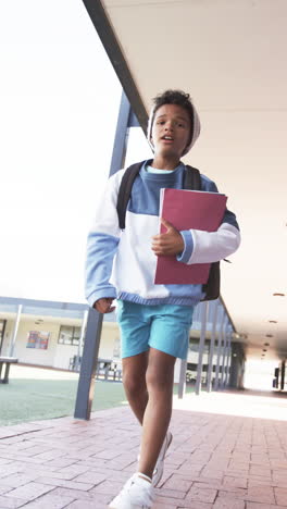 vertical video: in school, child walking with backpack and holding folder, looking ahead