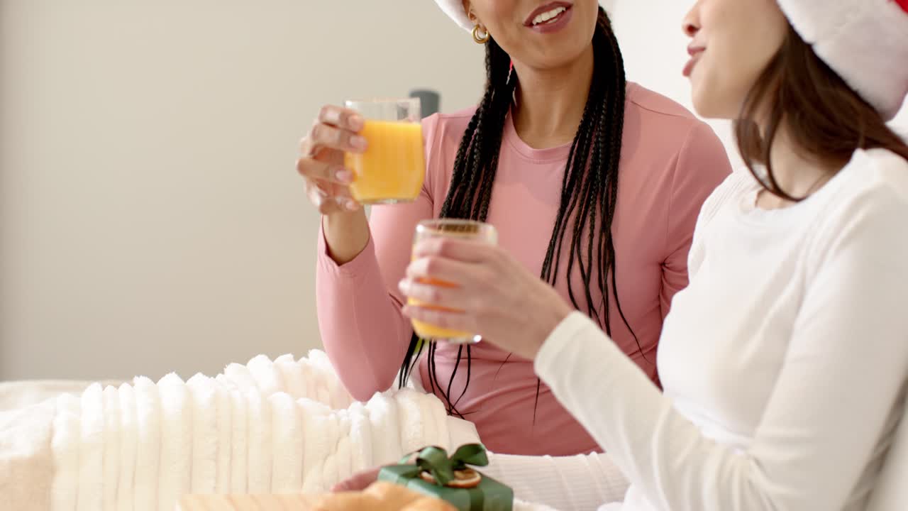 Diverse amiche in cappelli da Babbo Natale festeggiano brindando con succo d'arancia a letto con croissant in regalo