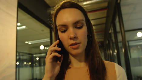 vista frontal de una joven mujer de negocios caucásica hablando por teléfono móvil y caminando en una oficina moderna 4k