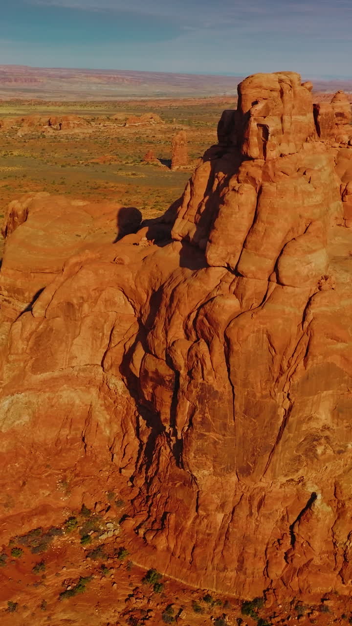 Bright sun lighting the orange mountain. Drone footage around the rock in the deserted landscape. Blue sky at backdrop. Vertical video