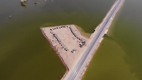 Vista-Aérea-Del-Campamento-Improvisado-Con-Tiendas-De-Campaña-Para-Albergar-A-Los-Refugiados-De-Las-Inundaciones-Al-Lado-De-Una-Carretera-Elevada-Rodeada-De-Aguas-Expansivas-En-La-Zona-Rural-De-Jacobabad,-Sindh