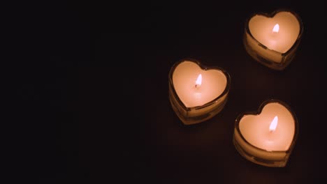 tres velas blancas en forma de corazón iluminadas en fondo negro que se están apagando