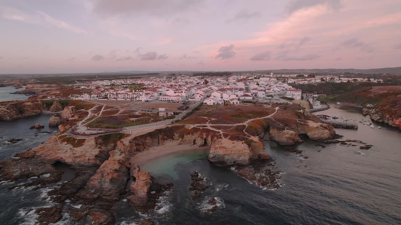 Il villaggio di Porto Covo si estende sopra scogliere rocciose atlantiche e insenature turchesi lungo la Costa Vicentina in Alentejo, Portogallo; drone che si allontana e orbita in campo largo.