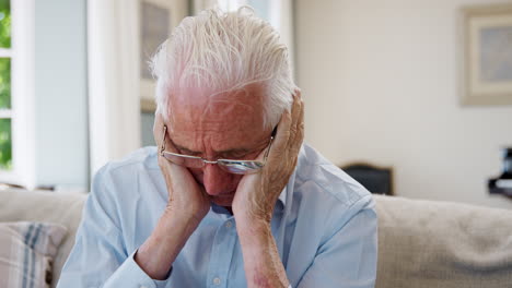 senior man sitting on sofa at home suffering from depression