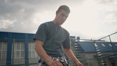 athlete bouncing volleyball outdoors with his right hand, sunlight creating silhouette effect around him, with a blue building and fence visible in the background