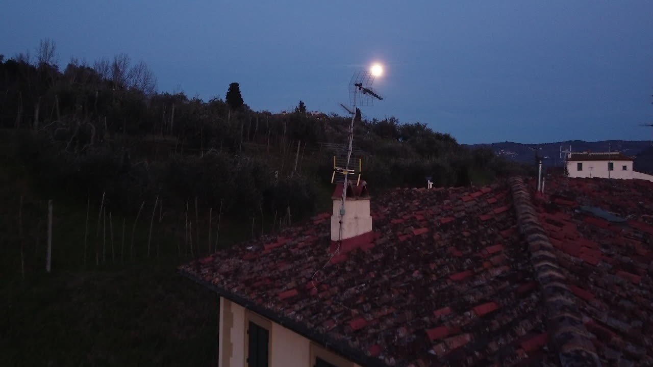 Un drone vola al tramonto sopra le case lungo il fiume Arno mentre la luna piena sorge nel cielo nella piccola città di Girone, vicino a Fiesole, Firenze, nella regione Toscana d'Italia. Dicembre 2019