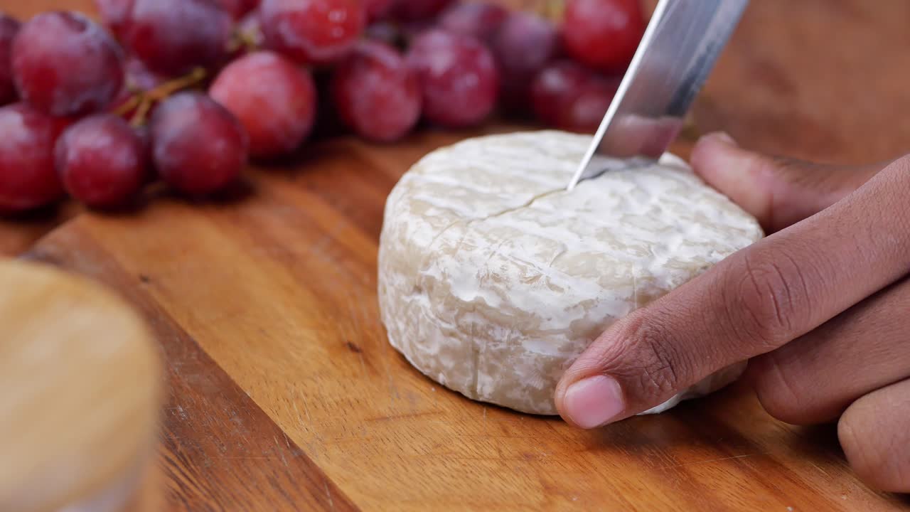 cortando una rueda de queso camembert con uvas
