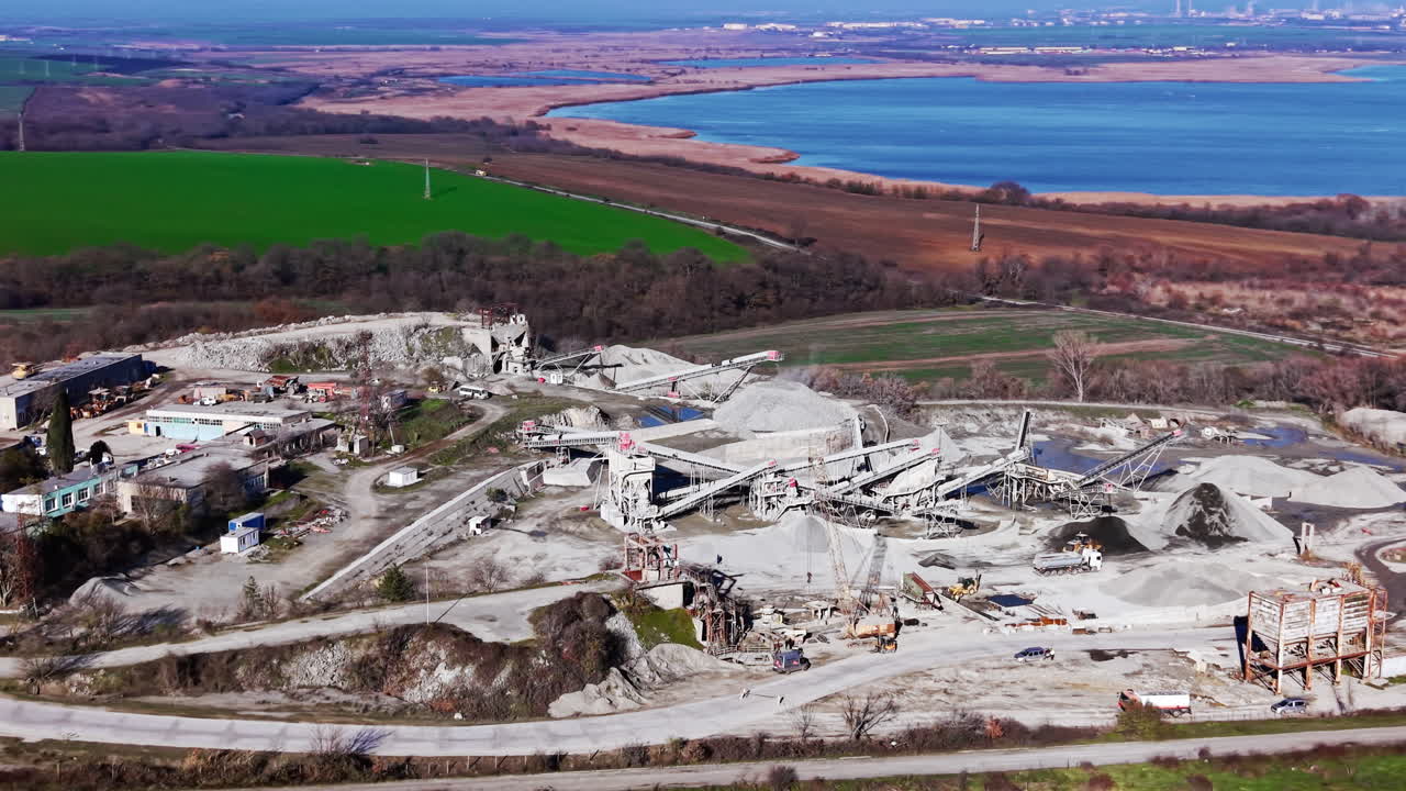Grootschalige industriële mijnbouwfaciliteit met transportbanden en voorraden gelegen in een landelijk landschap. Breed luchtpanorama van granietgroeve nabij meer.