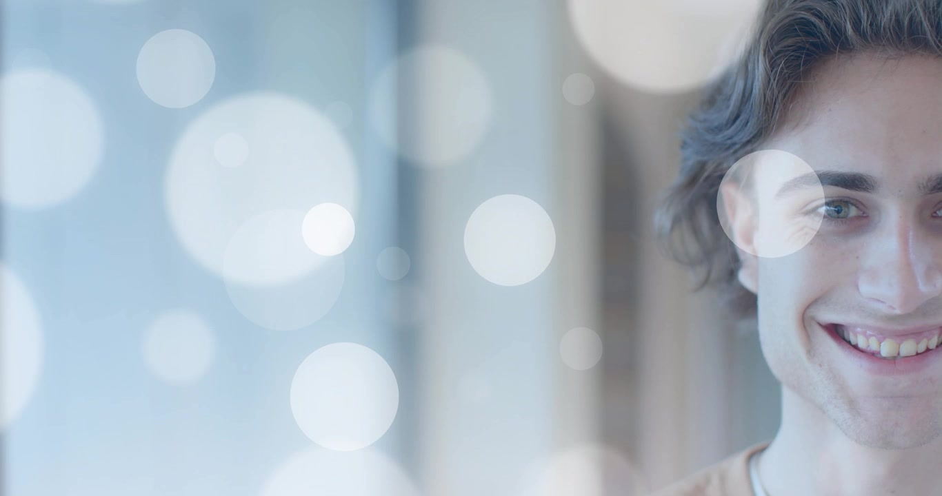 Uomo accanto alla finestra che vede forme bokeh fluttuanti illuminargli il viso e rivelare un sorriso per il marketing