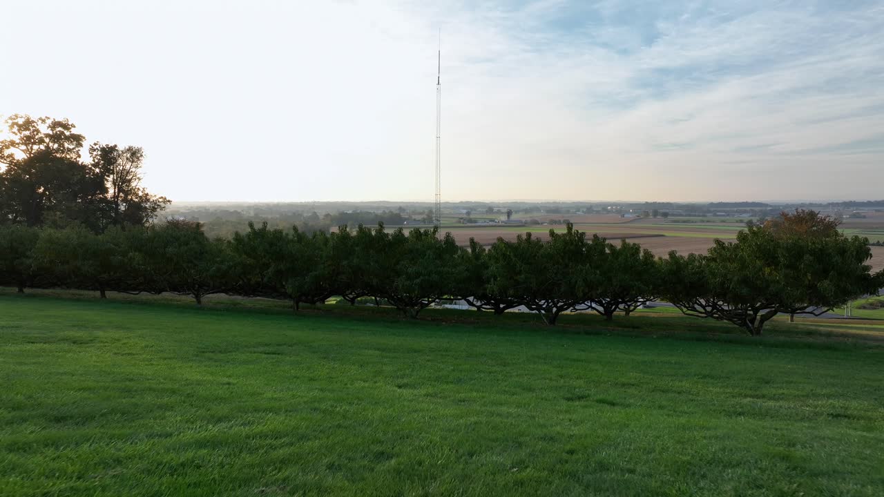 Hills grass in garden of American farmstead house in USA. Sunset time in fall season. Farmland fields with cultivation in the valley of town. Wide shot. Drone forward shot