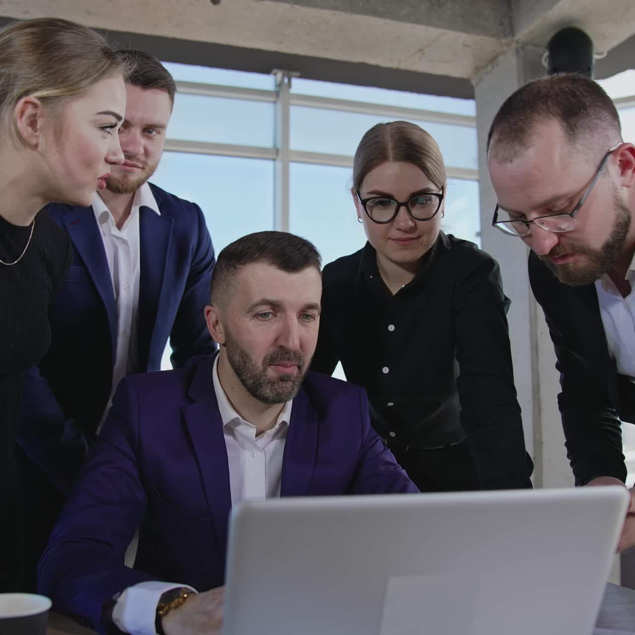 Business team standing around the chief and looking at laptop. One of the male colleagues showing his smartphone