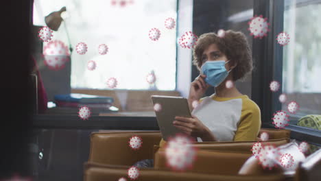 animation of covid 19 cells over woman in office using tablet and wearing face mask