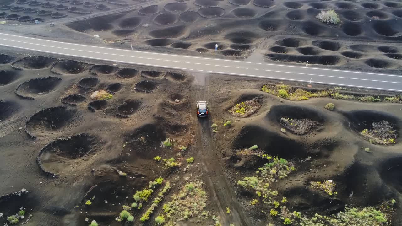vehículo que sale del camino de tierra a la carretera pavimentada en la granja del cráter con uvas en lanzarote, vista aérea
