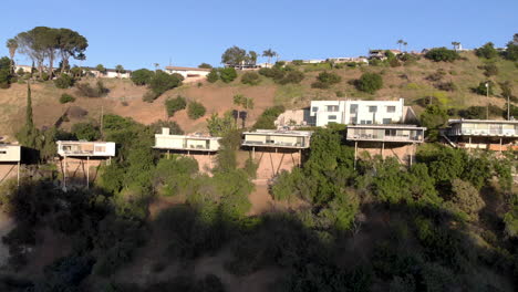 aerial flyby of homes on stilts hanging off cliffs of a mountain overlooking a valley city