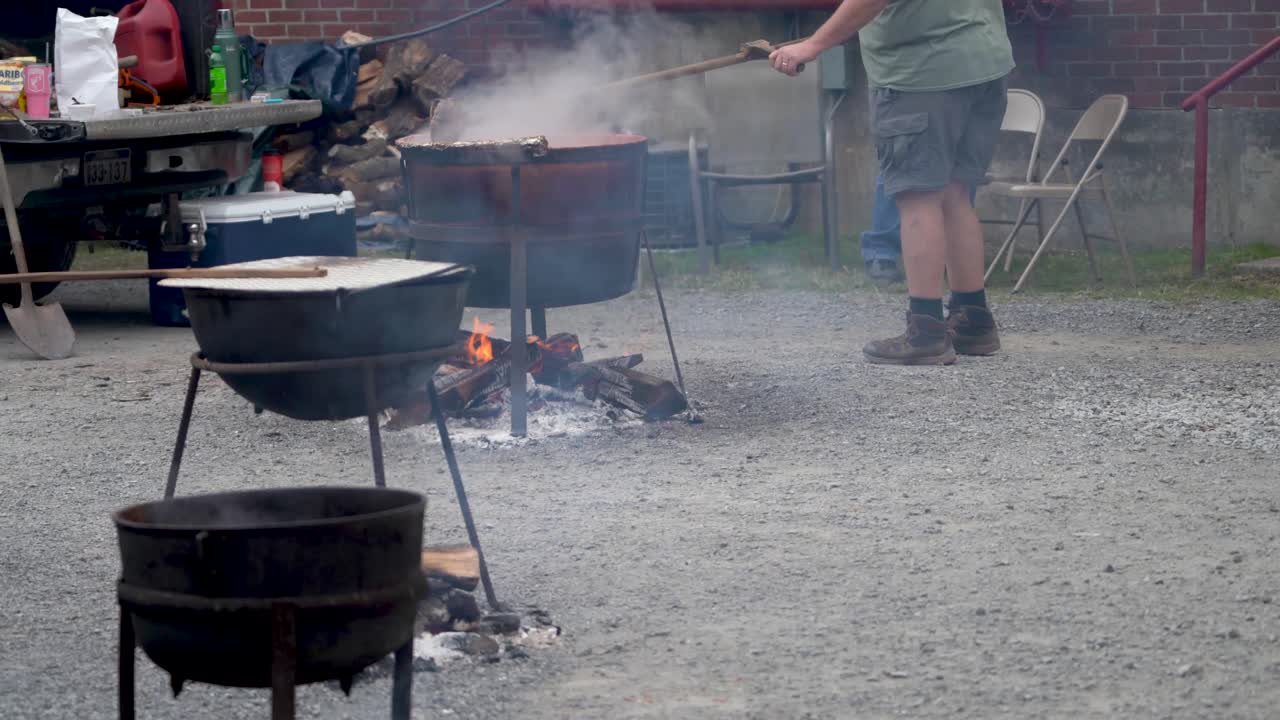 한 남자가 그 중 하나에 사과 버터를 는 동안 여러 개의 검은 카델론이 연기하고 증기가 나 있는 나무 불과 함께