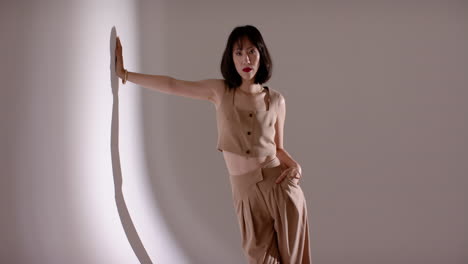 following cues chinese female in tan outfit stepping in spotlight, reflecting on grey wall