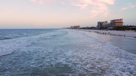 Excelente-Vista-Aérea-De-La-Gente-Caminando-A-Lo-Largo-De-La-Orilla-De-La-Playa-De-New-Smyrna,-Florida-Al-Atardecer