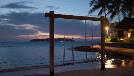 Pair-of-Empty-Rope-Swings-at-Sunset-Beach-By-the-Sea-at-Tropical-Island,-Bungalow-with-Street-Lights-And-Palms---Exotic-Luxury-Resort-Template