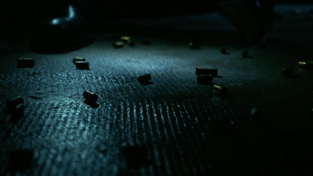Man in Black Suit Sits on a Floor Full of Gun Shell Casings with Flicking Lights