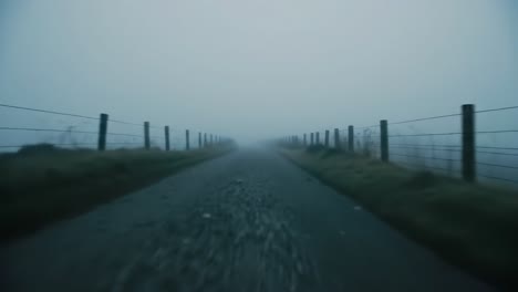 a winding gravel road cuts through a foggy rural landscape at dawn. the atmosphere is tranquil, with low visibility created by thick mist, showcasing nature's quiet beauty.