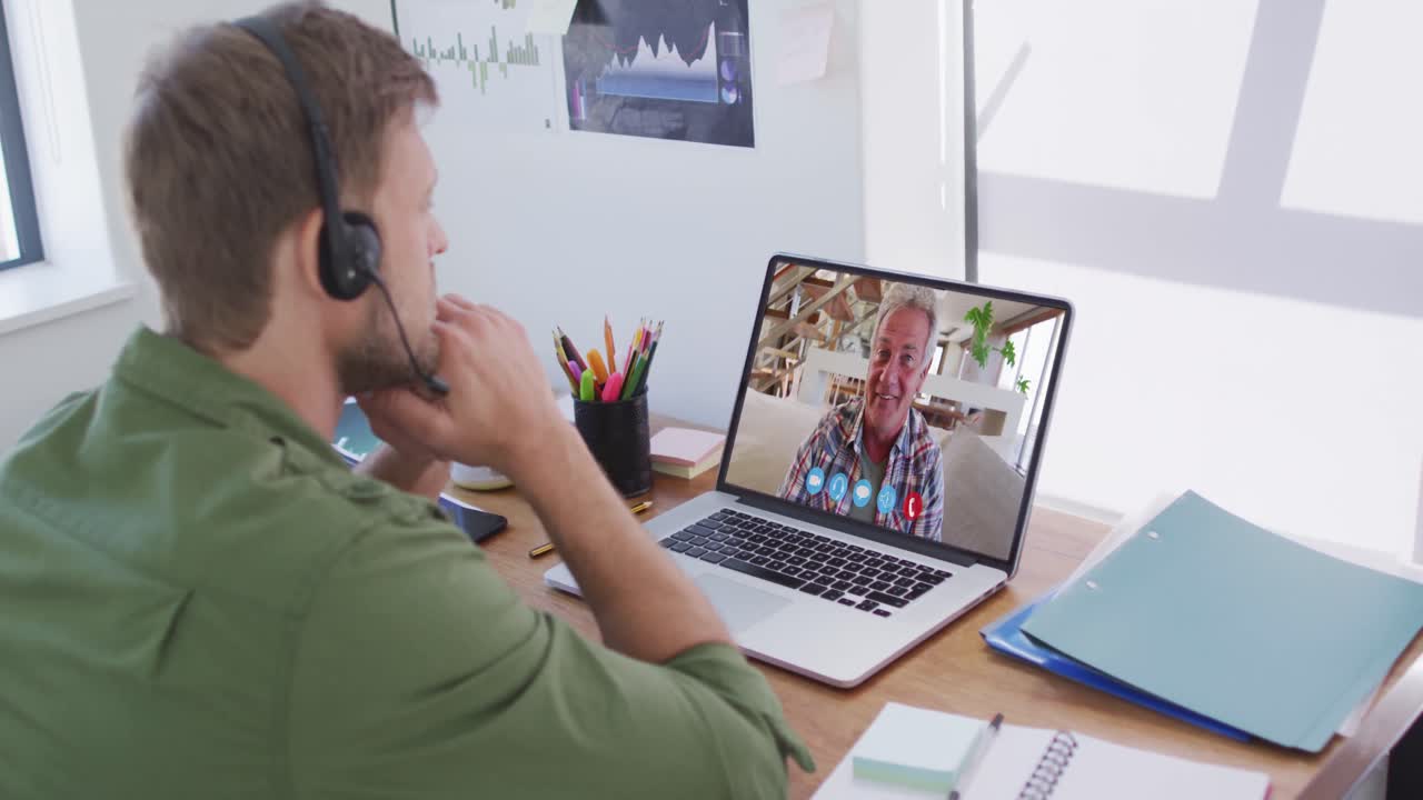 Kaukasisk mand i en videochat på en bærbar computer, iført telefonheadset derhjemme.