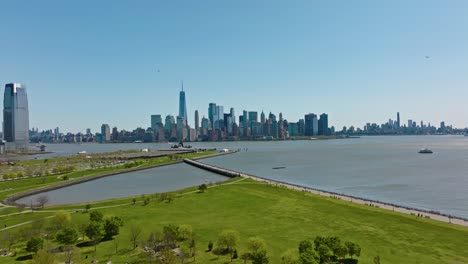 Aerial-backwards-shot-over-Green-Liberty-State-Park-with-Manhattan-Skyline-of-NYC-in-background---Beautiful-sunny-day-with-blue-sky-in-USA