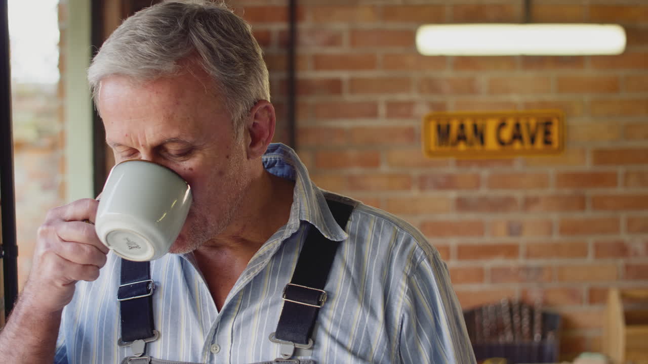 retrato de un hombre maduro vestido con mono en un taller de garaje con una bebida caliente