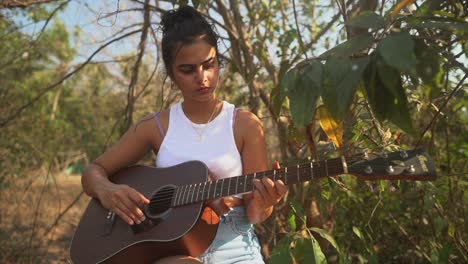 indian girl playing the guitar during sunset in the middle of a green field