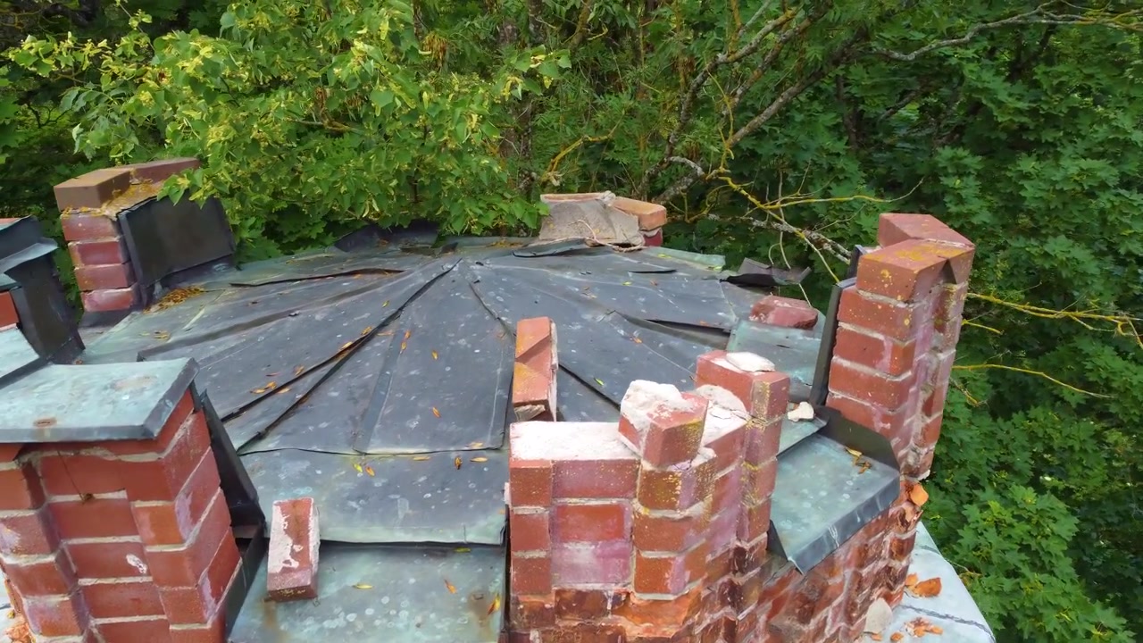 Weathered brick chimney surrounded by lush green trees in a forested area, aerial view