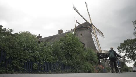 Young-Dutch-Woman-Walking-With-a-Bike-Past-next-to-a-Windmill