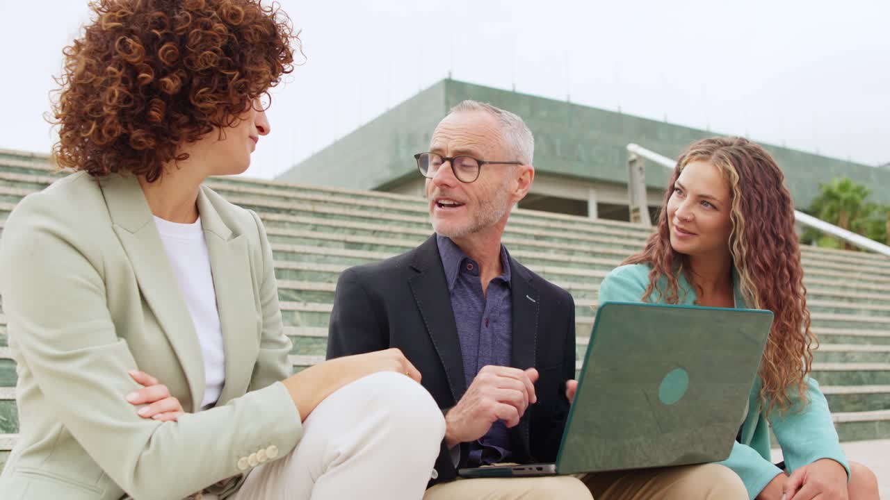 Group of business people sitting on the steps of the building and working on a laptop