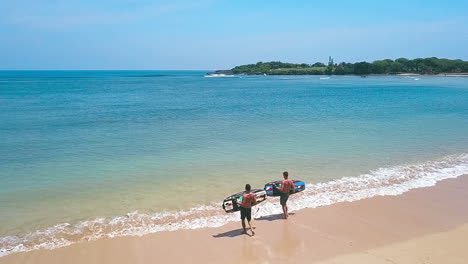 two young men taking jetsurf boards out on a beautiful beach in bali, slow motion