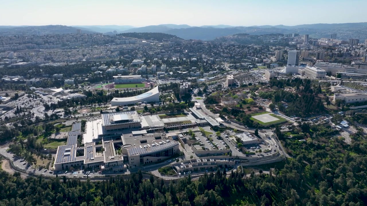 Vista aerea grandangolare del campus Givat Ram dell'Università Ebraica circondato da colline verdi di pineta e skyline urbano a Gerusalemme