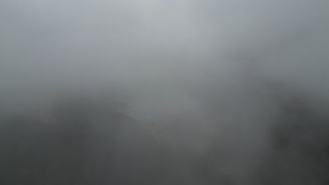 aerial pullback between misty clouds hides reservoir lake in alpine mountain region