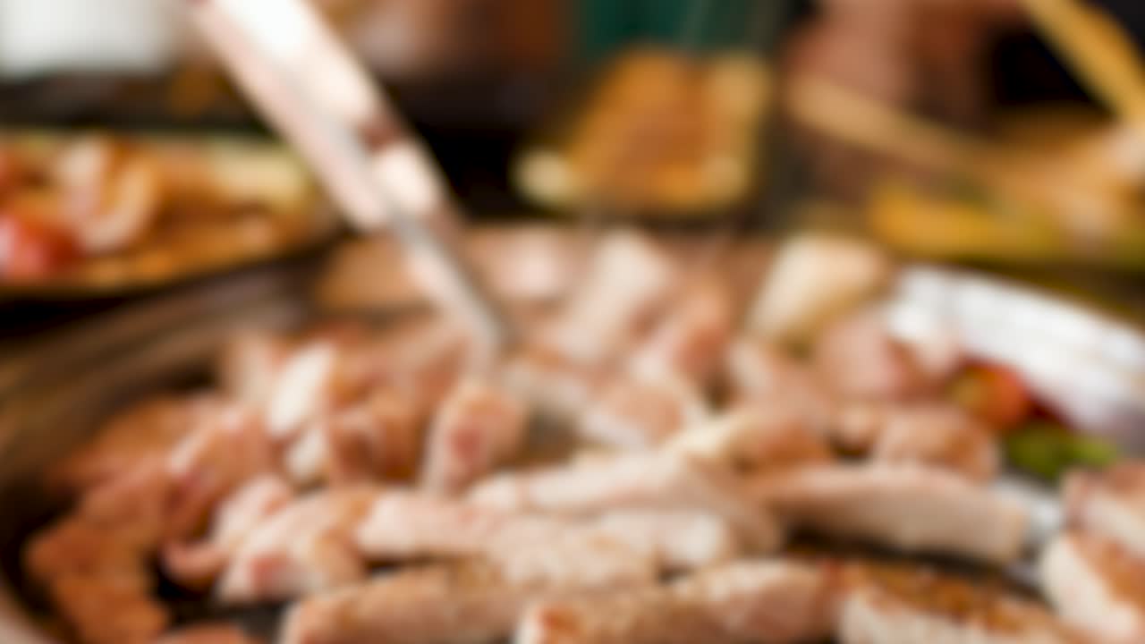 Hand uses tongs to turn pork slices on hot grill pan, steam rising indoors