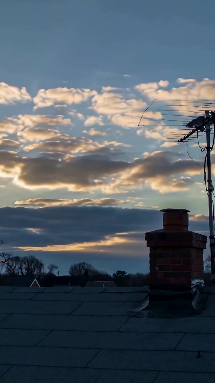 Video verticale: Inquadratura di un camino in mattoni e un'antenna TV sul tetto mentre il sole delinea le nuvole, spazio per il testo