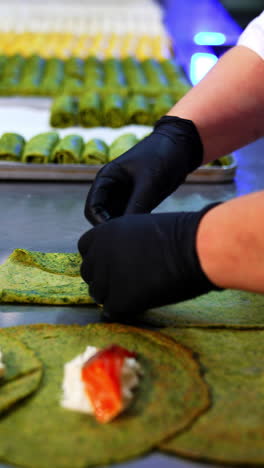 chef in black gloves preparing pancakes with stuffing. green crepes are rolled with fish and cheese inside. close up. vertical video