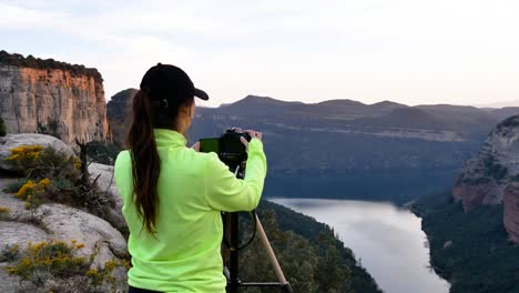 young woman photographing mountains on camera placed on tripod