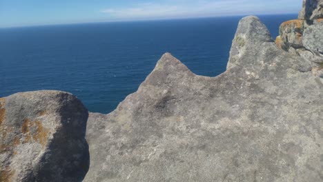 the atlantic ocenae is discovered behind the eroded granite rocks of the cliff on a sunny day, crane shot rising, cíes islands, pontevedra, galicia, spain