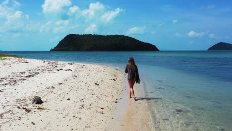 Mujer-Solitaria-E-Irreconocible-Caminando-Por-Una-Playa-De-Arena-Blanca-Junto-A-Aguas-Tranquilas-Y-Claras-De-Una-Laguna-Poco-Profunda,-Islas-Tropicales-En-Tailandia