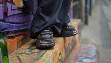 close up outdoor fashion shot shoes and clothes of alternative style woman against graffiti covered wall in london city street uk in real time