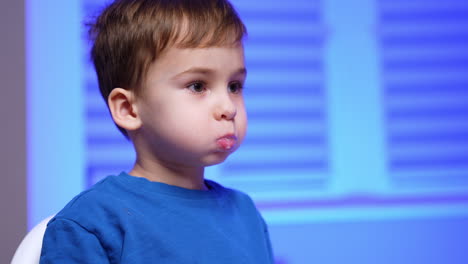 toddler boy is holding dairy in his mouth. baby boy points at something aside. little kid drinks dairy from the bottle. close up portrait.
