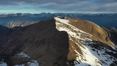 Aerial-view-over-mountain-ridge-with-snow-on-one-side,-Italian-alpine-landscape