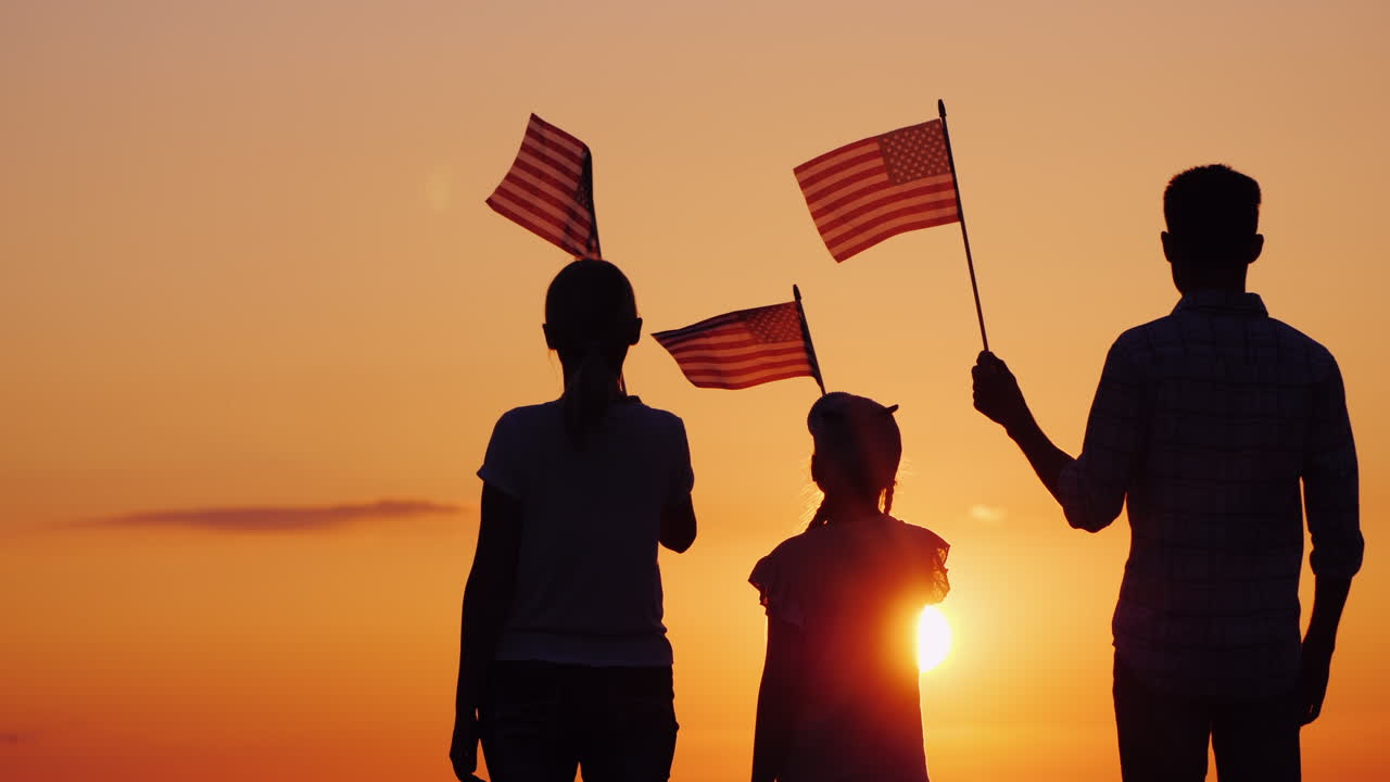 familia feliz con un niño que nos ondea banderas al atardecer vista trasera
