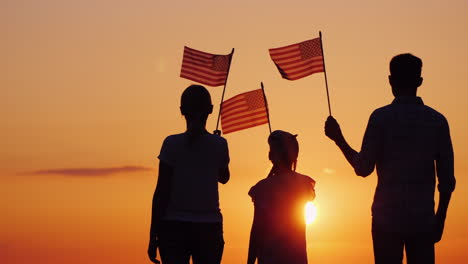 Glückliche-Familie-Mit-Kind,-Die-Uns-Fahnen-Bei-Sonnenuntergang-Rückansicht